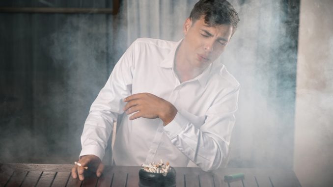 Young,Guy,Fending,Off,Tobacco,Smoke,,Sitting,At,A,Table